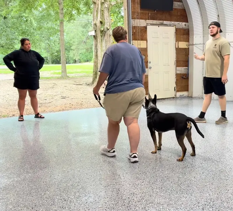 Bailey Clark coaching two owners inside a covered shop while one handles their heeler mix on leash